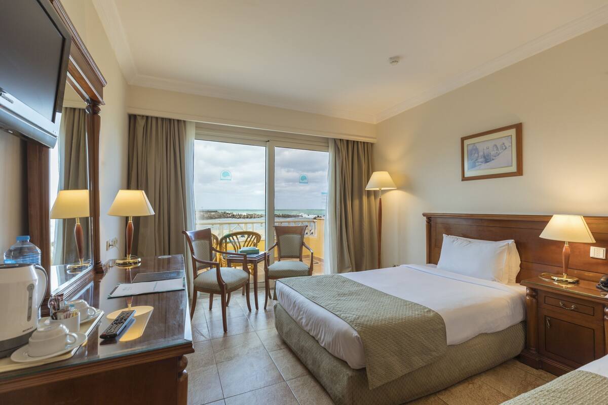 Une chambre d’hôtel comprenant un lit, des tables de chevet, un bureau avec une chaise, une fenêtre avec des rideaux et une vue sur l’extérieur.