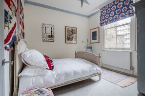 Un dormitorio con cama, ventana con vistas a edificios, radiador y cortina estampada.