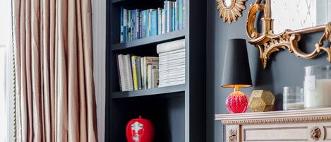 Una habitación con una estantería negra, un jarrón rojo, una chimenea y una silla rosa.