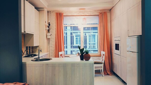 A modern kitchen with a central island, white cabinetry, and a view of buildings through large windows. - MalinaApt Alice in Wonderland (Kyiv)