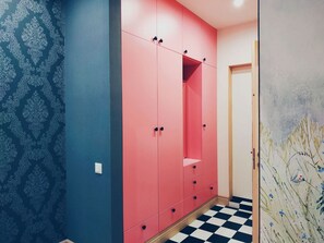 Un couloir doté d’un sol à carreaux, d’une armoire rose à plusieurs portes et d’un papier peint à motifs sur un des murs.