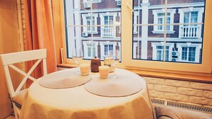 A cozy room with a table set for two, a window with a view of brick buildings, and a radiator below the window. - MalinaApt Alice in Wonderland (Kyiv)