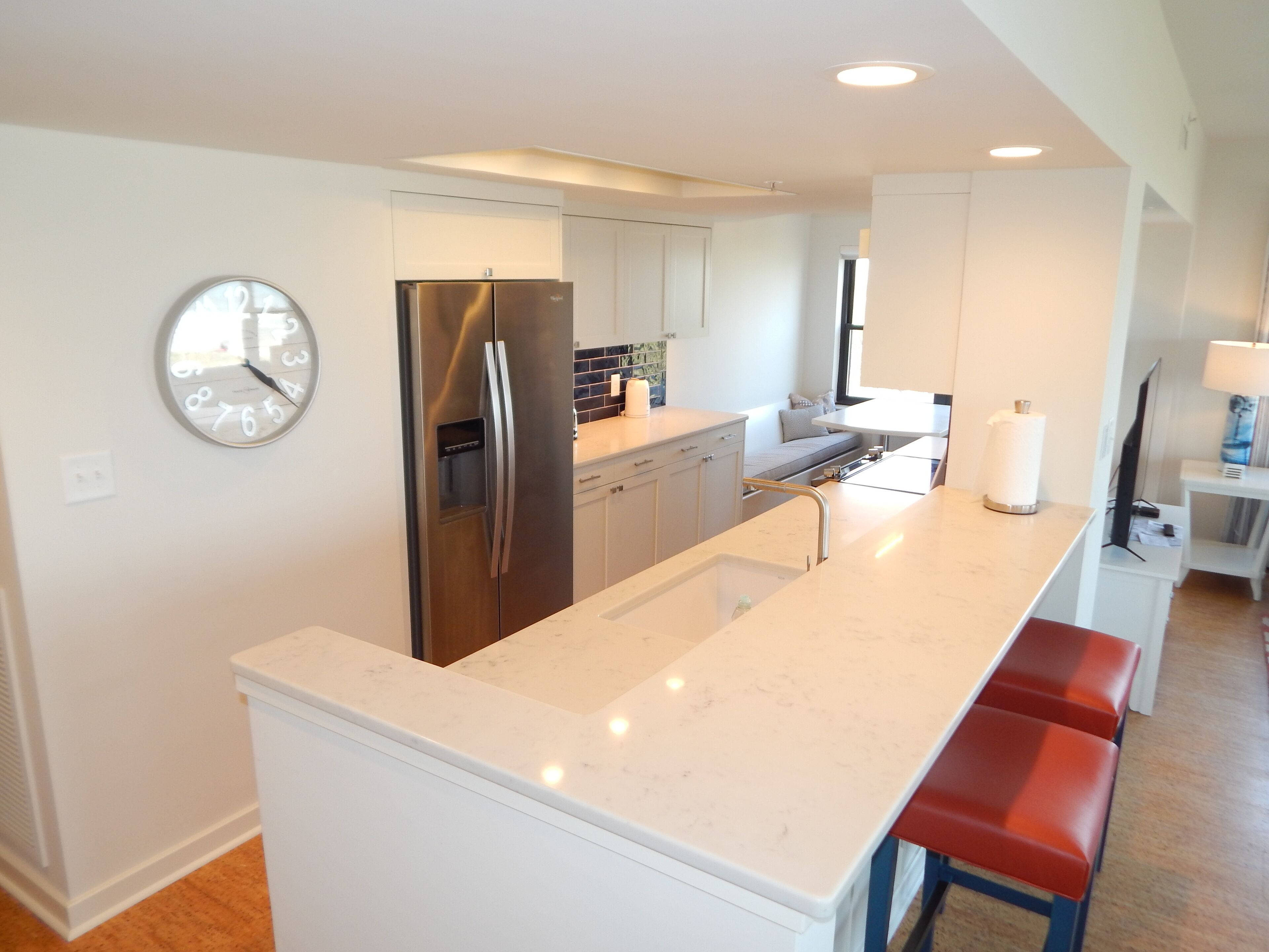 Una cocina moderna con refrigerador de acero inoxidable, armarios blancos, encimera de mármol y horno empotrado.