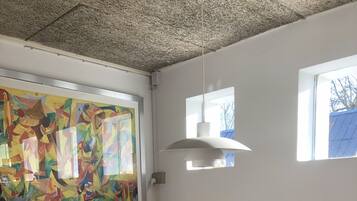A dining area with a white table, four chairs, a ceiling with a textured pattern, a hanging light fixture, and a colorful abstract painting on the wall.