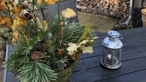 A wooden deck with a metal lantern, a stack of firewood, and a potted plant with pine branches and leaves.