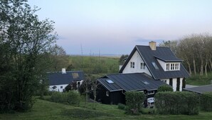 A rural house with a sloped roof, surrounded by greenery and a clear sky.
