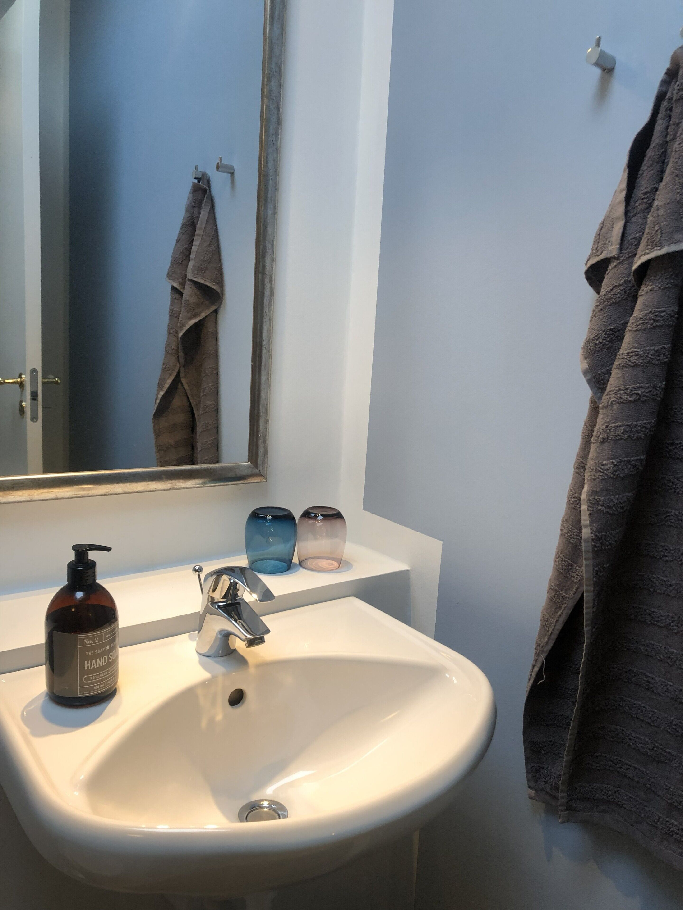 A bathroom with a white sink, a mirror, a towel rack, and a soap dispenser.