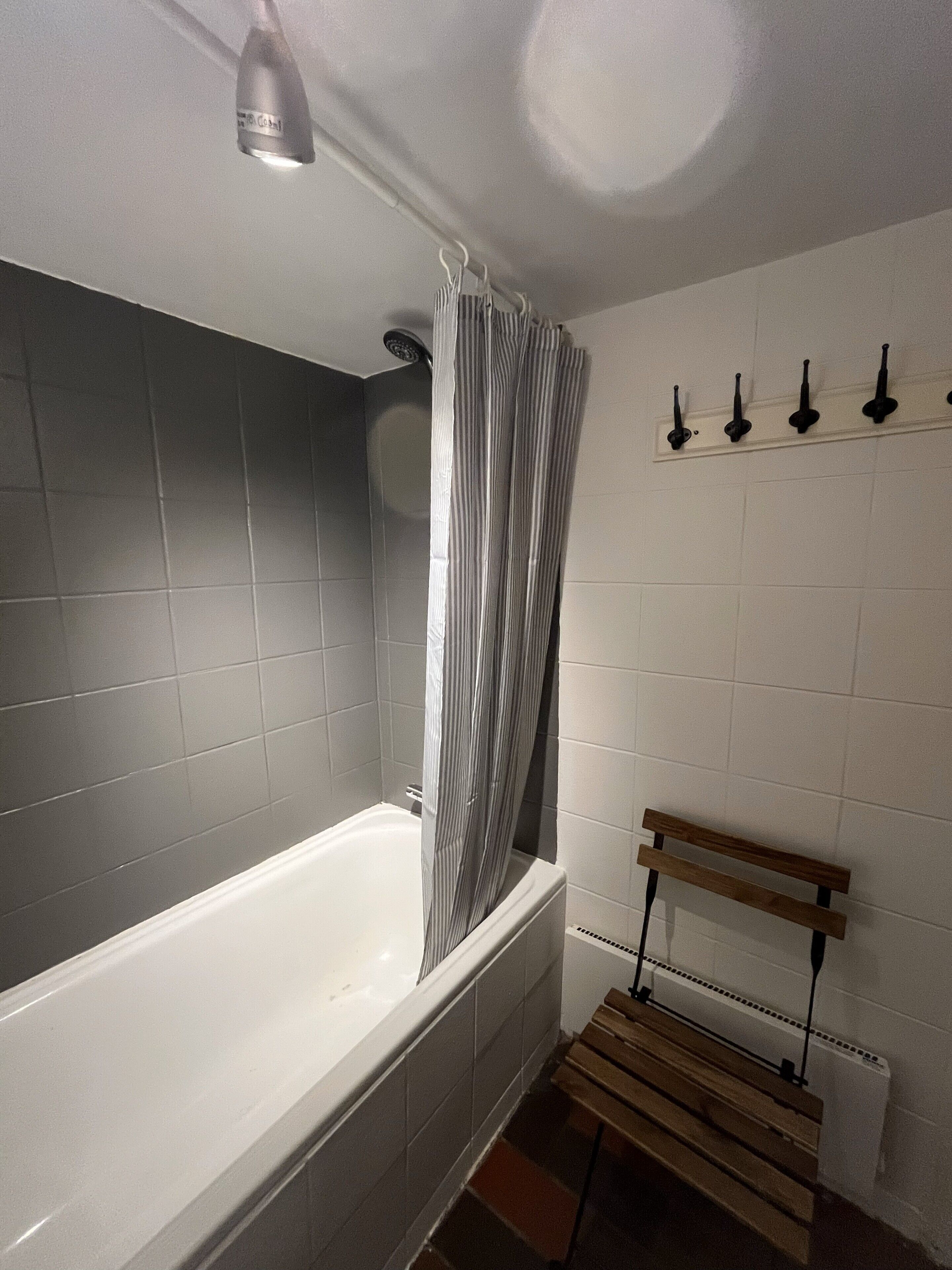 A bathroom with a bathtub, a shower, a wooden bench, and a towel rack.