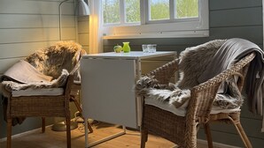 A room with two wicker chairs, a small white table, a lamp, and a window with a view of trees.
