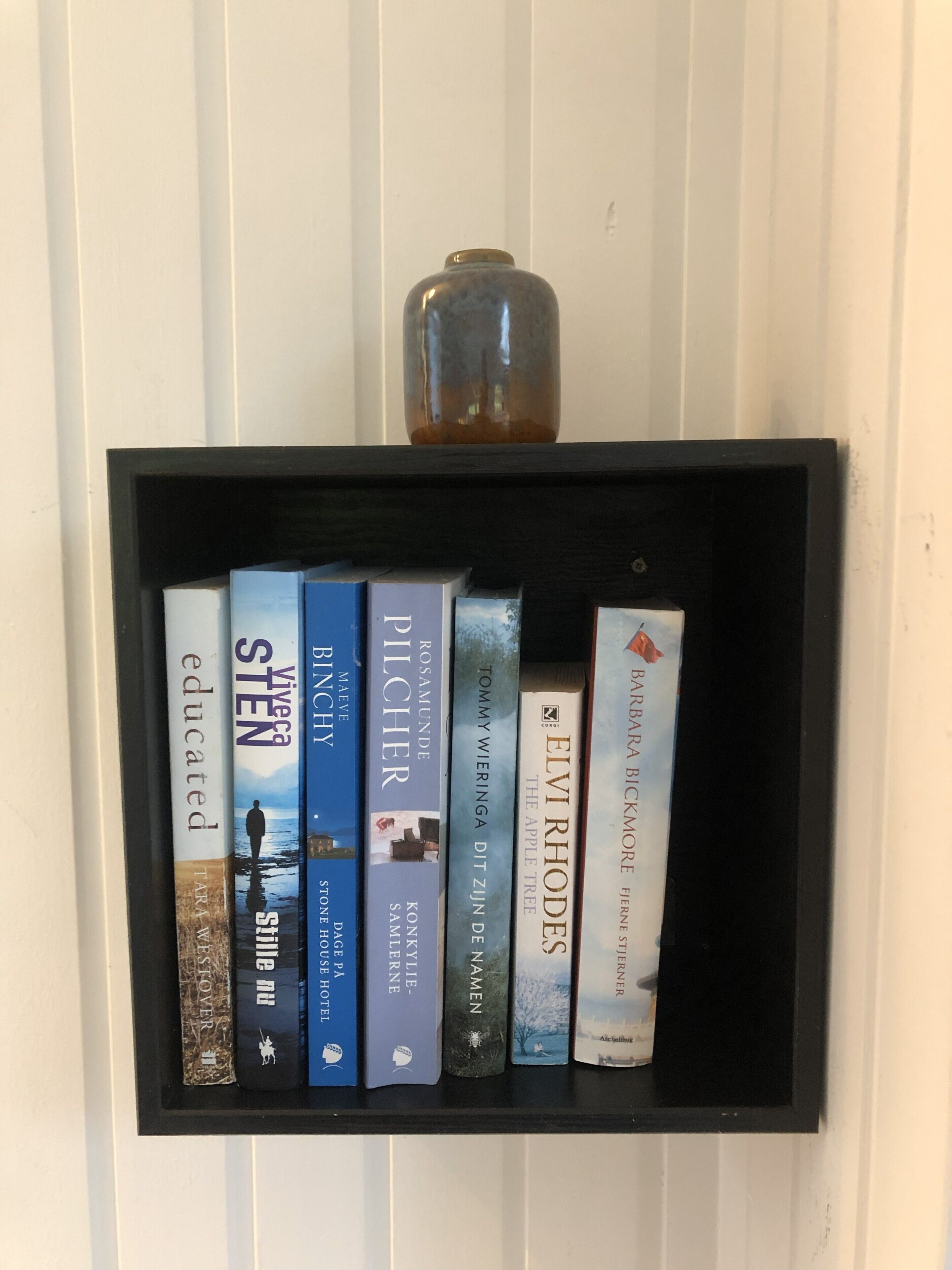 Una libreria nera con sei libri e un piccolo vaso sopra.