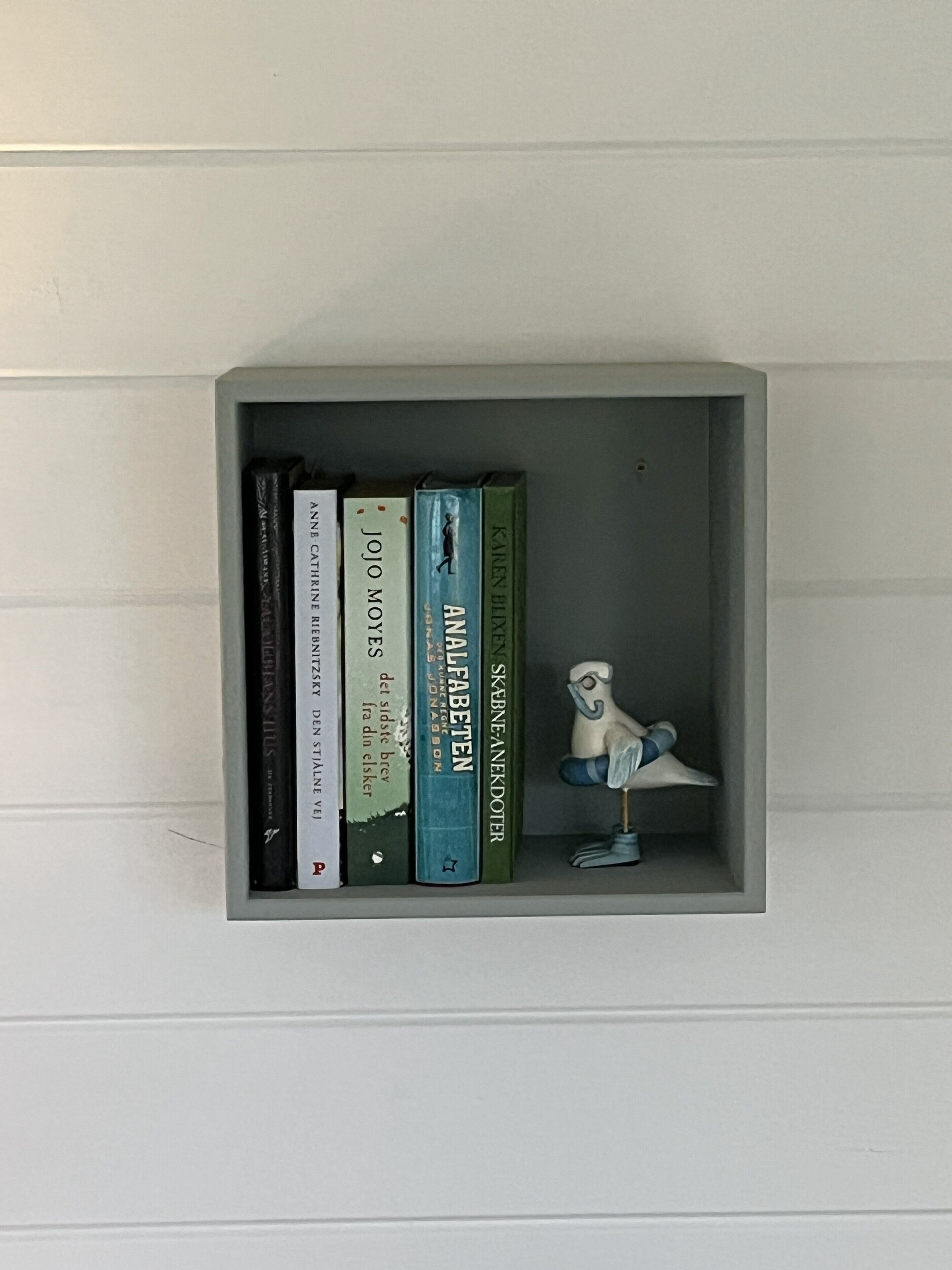 Una estantería con libros y una pequeña figurita de pájaro.