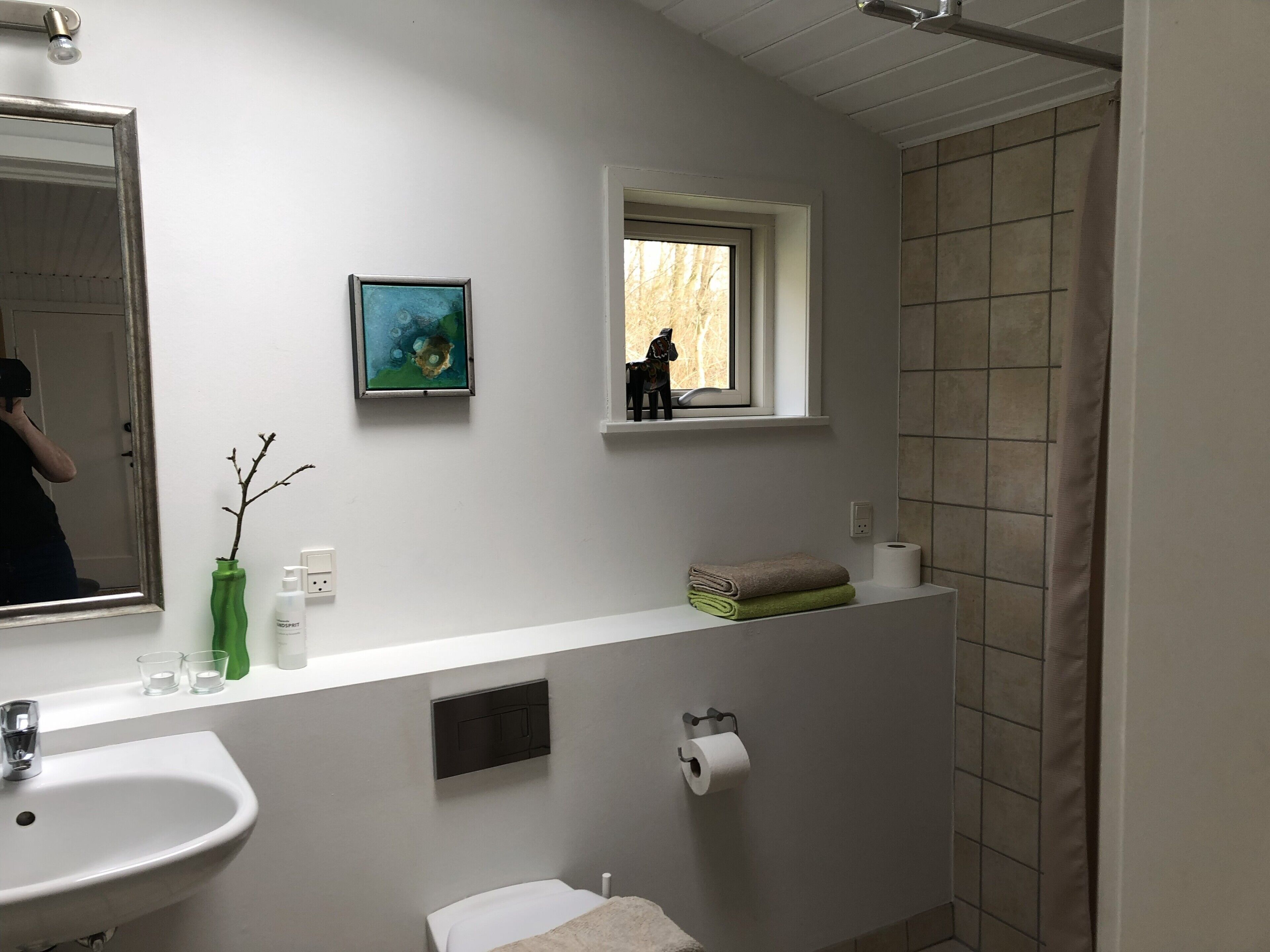 Un baño con lavamanos, espejo, ventana, toalla, papel higiénico y cortina de ducha.