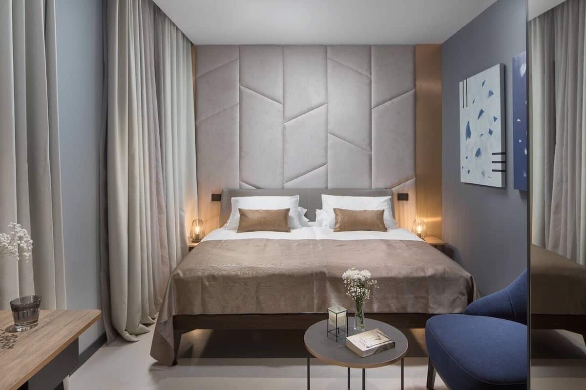 Una habitación de hotel moderna con una cama grande, una mesita redonda y un sillón azul.