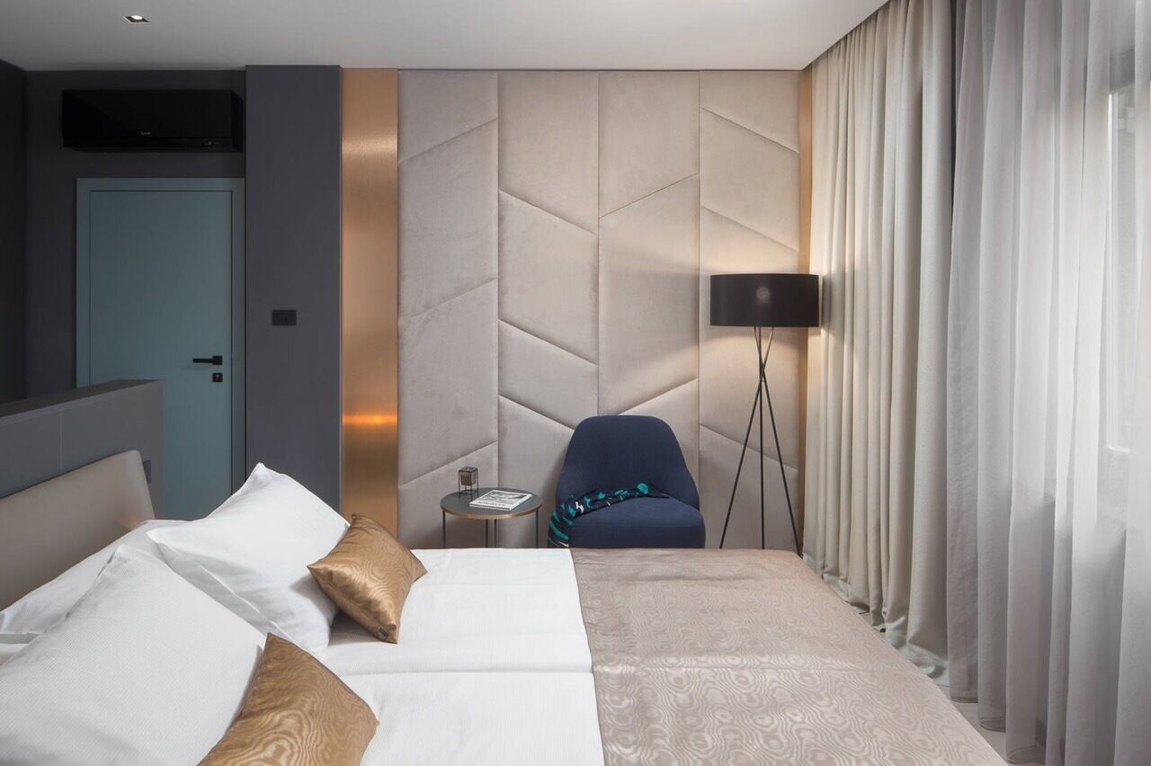 Une chambre d’hôtel avec un lit, une chaise, une petite table, un téléviseur fixé au mur et une porte.