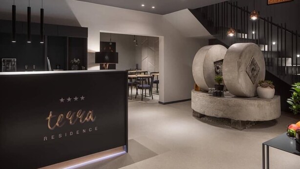 A modern reception area with a black counter, a staircase, and a dining area in the background. - Terra Residence (Labin)