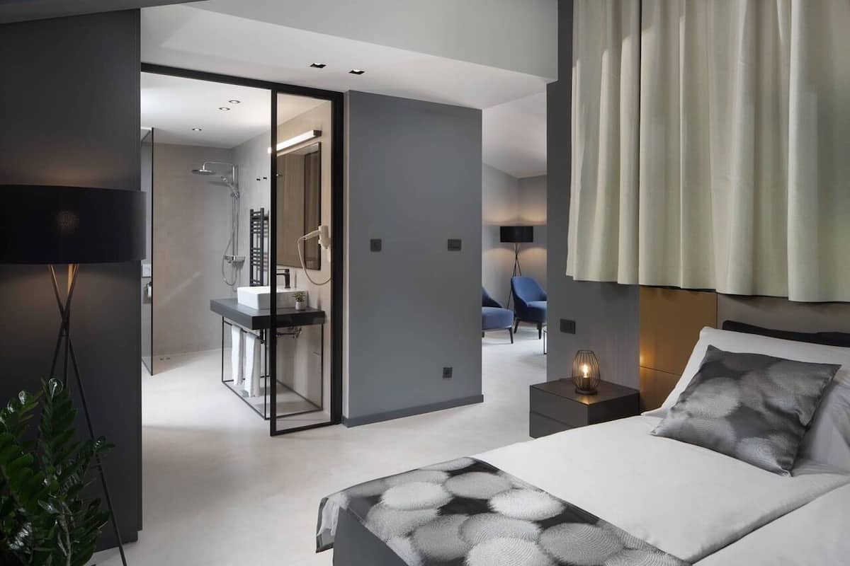 Habitación de hotel moderna con una cama grande, una mesita de noche, una lámpara y vistas al baño.