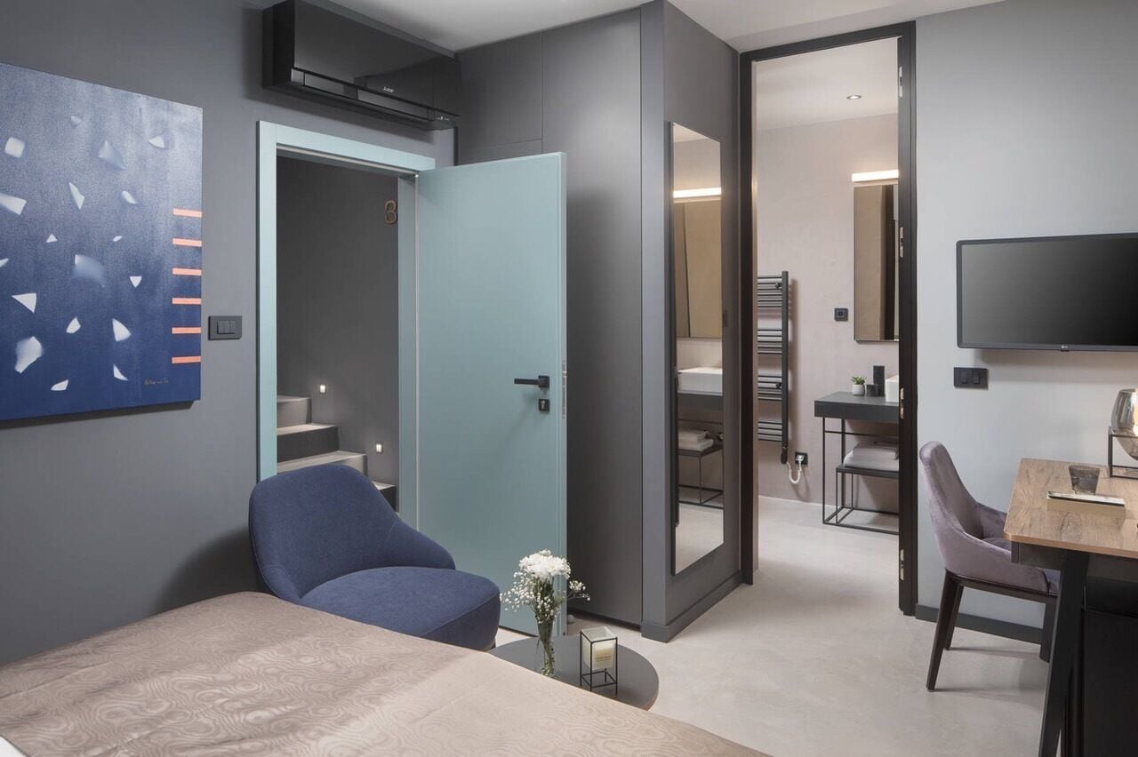 Ein modernes Hotelzimmer mit einem Bett, einem Schreibtisch, einem Stuhl, einem Fernseher und einem durch eine geöffnete Tür einsehbarer Badezimmer.