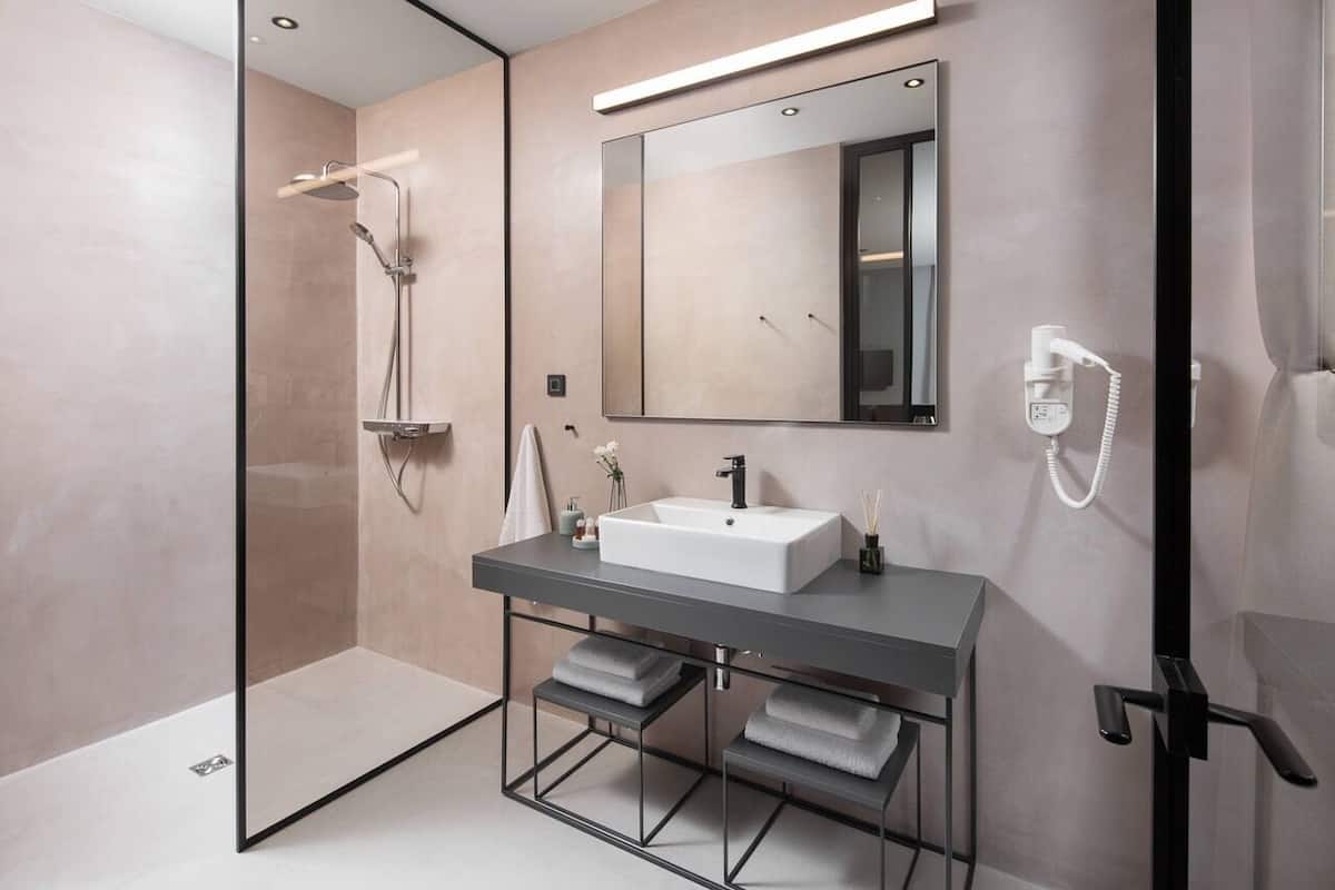 Un baño moderno con ducha de vidrio, un espejo grande, un lavabo blanco y un perchero para toallas.