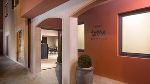 A hotel entrance with a modern design, featuring a red wall with the name 'terra' and a sign indicating 'RESIDENCE HOTEL'. There are two large planters with shrubs in the foreground. - Terra Residence (Labin)