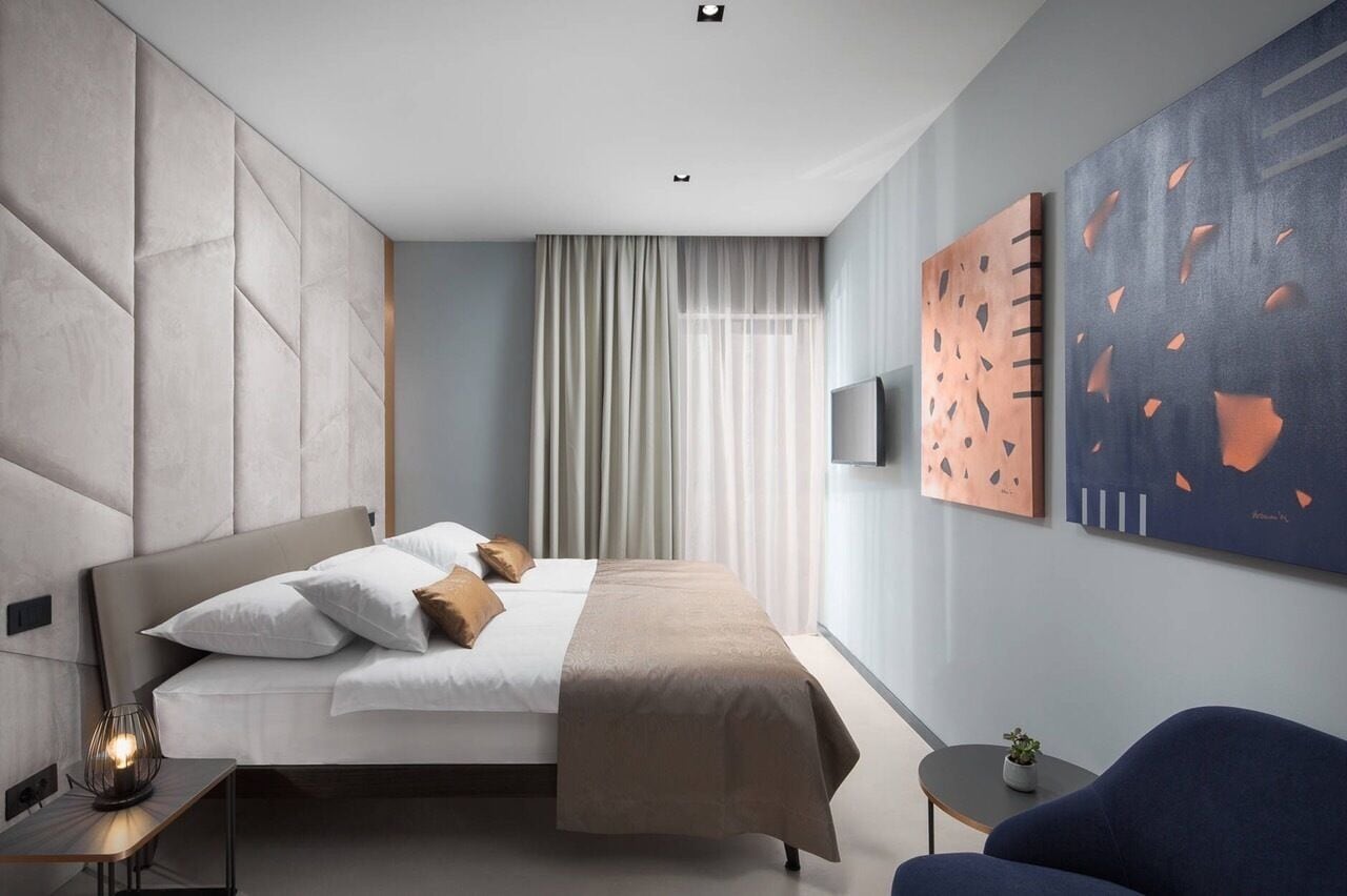 A modern hotel room with a large bed, a bedside table, a chair, and a TV.