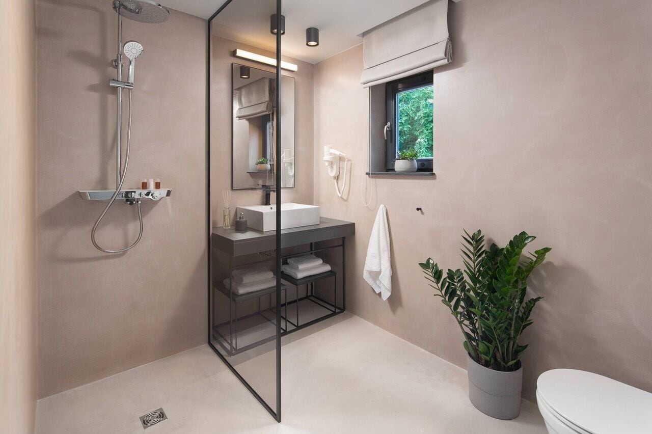 A modern bathroom with a glass-enclosed shower, a white sink, a toilet, and a potted plant.