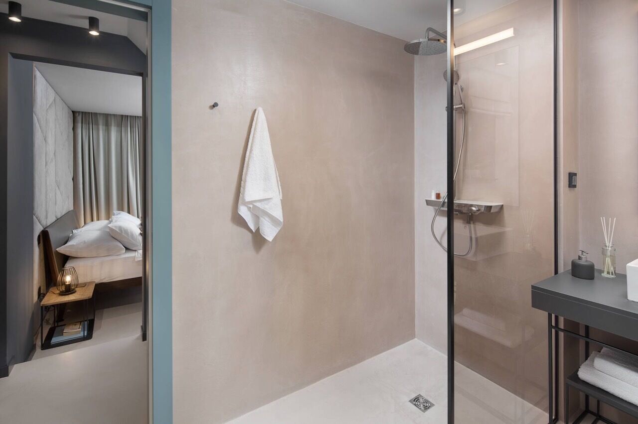 A modern bathroom with a glass shower enclosure, a bedside table with a lamp, and a towel hanging on the wall.
