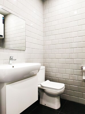 A bathroom with white subway tiles, a white sink, and a toilet.