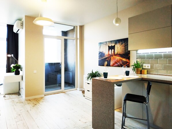 A modern kitchen with a large island, a dining area with a bar stool, and a sliding glass door leading to a balcony.