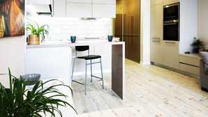 Una cocina moderna con armarios blancos, piso de madera y una barra con taburetes.