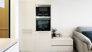 Una cocina moderna con horno y microondas integrados, una planta pequeña en la encimera y un sofá en la zona de estar contigua.