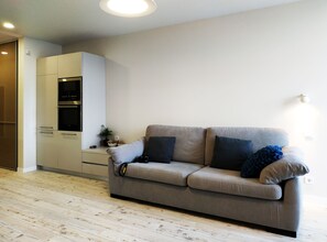 A modern living room with a grey sofa, a white cabinet, and a wooden floor.
