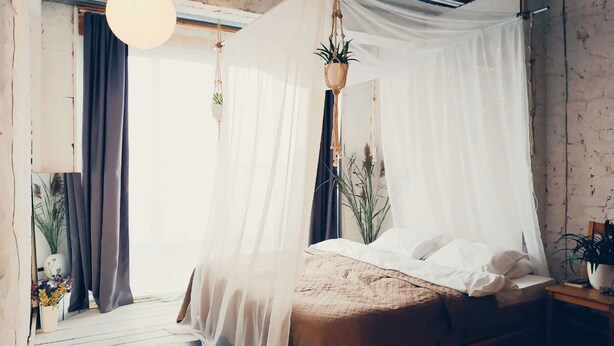 A bedroom with a bed under a canopy, a hanging plant, and a nightstand with a lamp. - MalinaApt  Bohemian Loft (Kyiv)