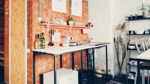 A kitchen with a brick wall, white cabinets, and a small refrigerator. There are shelves with kitchenware and a plant on the right. - MalinaApt  Bohemian Loft (Kyiv)