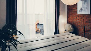 A room with a large window, a wooden table, a potted plant, a hanging paper lantern, and a brick wall with a framed picture. - MalinaApt  Bohemian Loft (Kyiv)