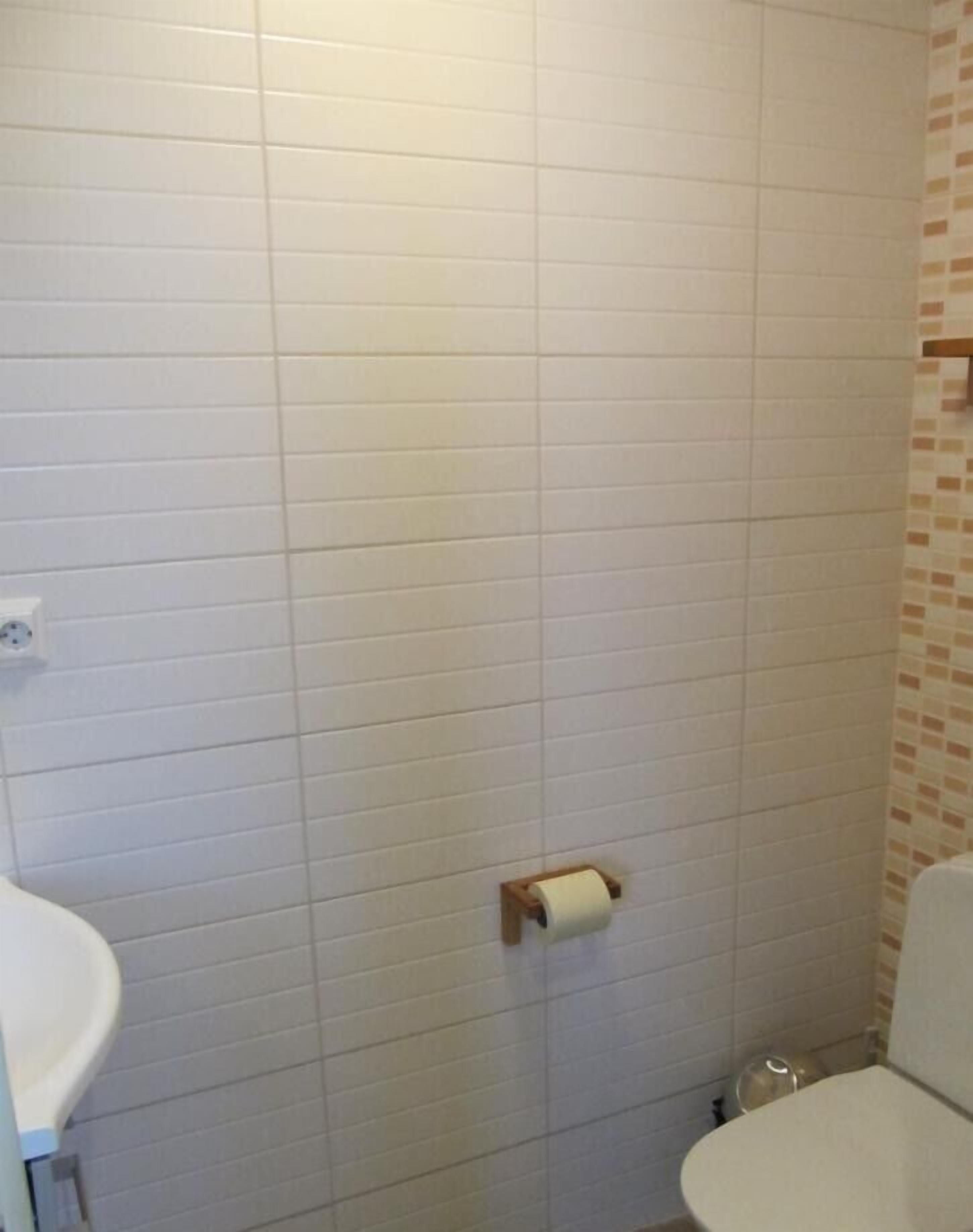 Un bagno con pareti piastrellate di bianco, un water e un portaserviti di carta.