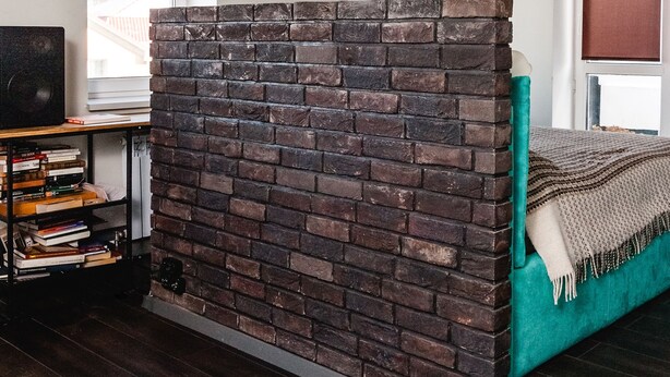 A room with a brick partition, a teal sofa, a wooden bookshelf, and a ceiling light fixture. - MalinaApt Mushka (Kyiv)