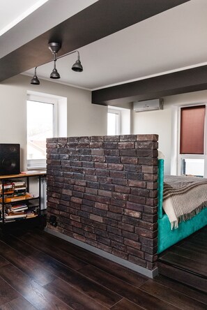 Ein Zimmer mit einer Ziegelscheibe, einem türkisblauen Sofa, einem Holzregal und einer Deckenleuchte.