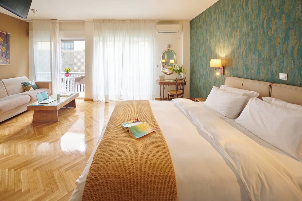 A hotel room with a bed, a sofa, a small table, a mirror, and a view of the balcony.