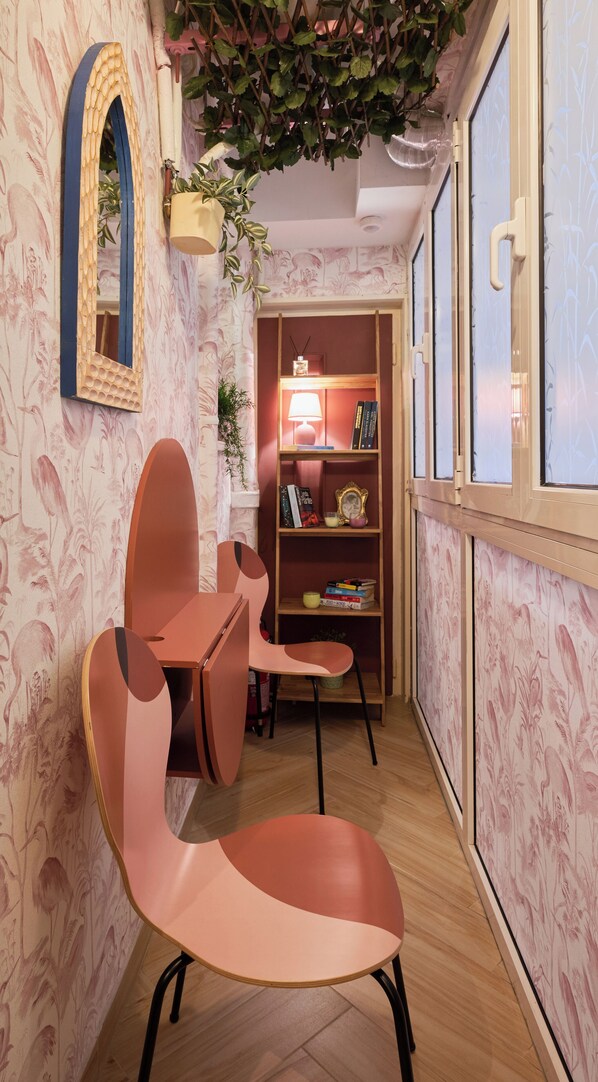 Une pièce avec un plancher en bois, une chaise rose, une bibliothèque et un miroir doté d’un cadre décoratif.