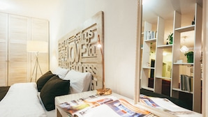 A neatly arranged bedroom with a bed, bedside table, lamp, and a wall with a decorative piece. - MalinaApt  Sophisticated red (Kyiv)