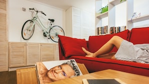 A person lying on a red couch with a magazine, a smartphone on a wooden table, and a bicycle mounted on the wall. - MalinaApt  Sophisticated red (Kyiv)