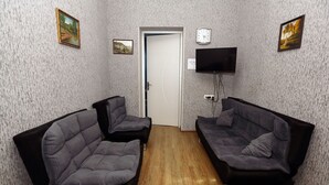 Ein Zimmer mit zwei dunklen Sofas, Holzboden, einer Tür und einem Fernseher an der Wand.