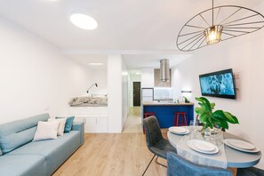 A modern living room with a sofa, dining table, and chairs. There is a kitchen area with a sink and a stove. A television is mounted on the wall. - MalinaApt Odri Dynamique (Kyiv)