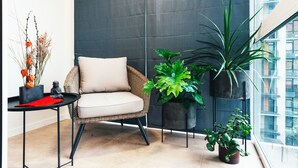 Un balcone con una sedia in vimini, piante in vaso e un tavolino con oggetti decorativi.