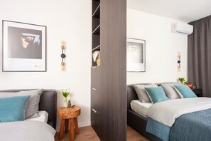 Une chambre d’hôtel moderne avec deux lits, une armoire, une petite table d’appoint en bois et un tableau encadré au mur.