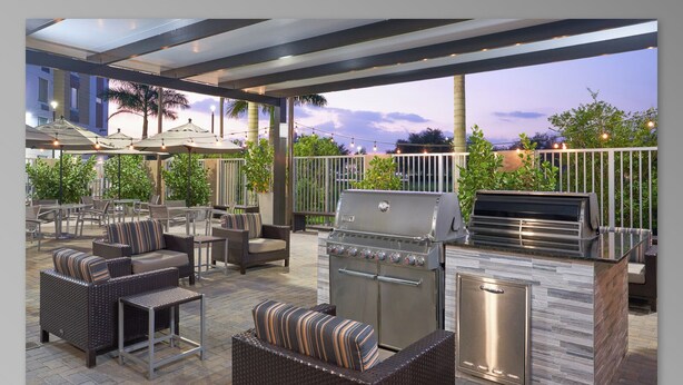 An outdoor patio with wicker furniture, a grill station, and a view of the city skyline at dusk.