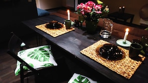 Een eettafel gedekt met placemats, kaarsen, een vaas met bloemen en een glas water.