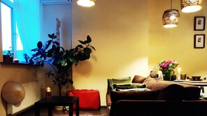 Een gezellige woonkamer met een bank, een rode fauteuil, een klein tafeltje, een plant en een gestreept vloerkleed.