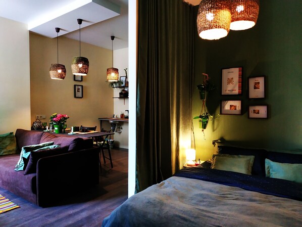 Ein modernes Zimmer mit Bett, Sofa, Esstisch und Pendelleuchten.