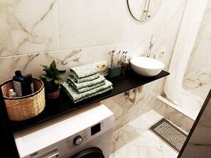 Ein modernes Badezimmer mit Marmorfliesenspiegel, Waschbecken, Spiegel und Waschmaschine.